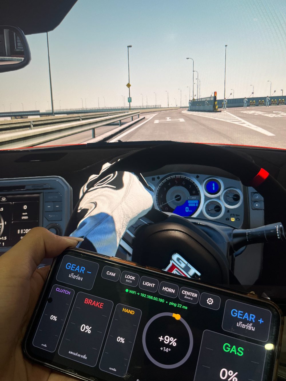 ถือมือถือที่เปิดแอพ ACWheel อยู่หน้าจอเกม Assetto Corsa รถหักพวงมาลัยตามมือถือ